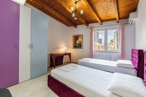 Ein Schlafzimmer mit zwei Betten, einem Schreibtisch, einem Gemälde und einem Fenster mit Blick auf die Stadt.