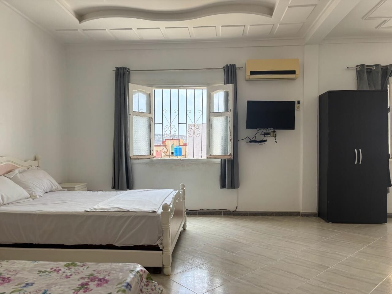 Un dormitorio con cama, armario, televisor y ventana con cortinas.