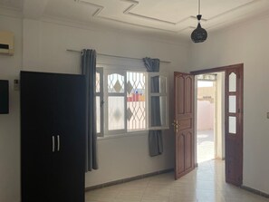 Una habitación con un armario oscuro, una ventana con cortinas, una puerta que da al exterior y un suelo de baldosas.