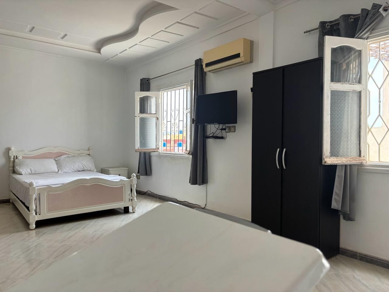 A bedroom with a bed, wardrobe, TV, and window with curtains.