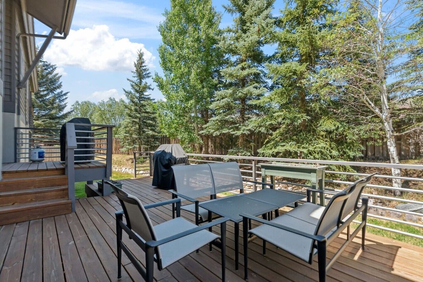 A deck with outdoor furniture, a grill, and a view of trees.