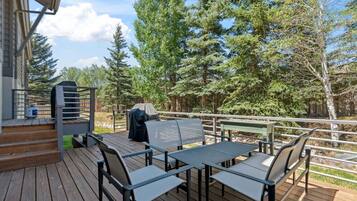 A deck with outdoor furniture, a grill, and a view of trees.