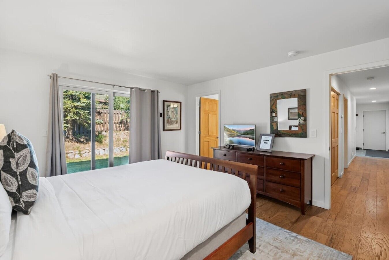 A bedroom with a bed, a dresser, a television, and a sliding glass door leading to a garden.