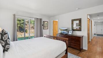 A bedroom with a bed, a dresser, a television, and a sliding glass door leading to a garden.