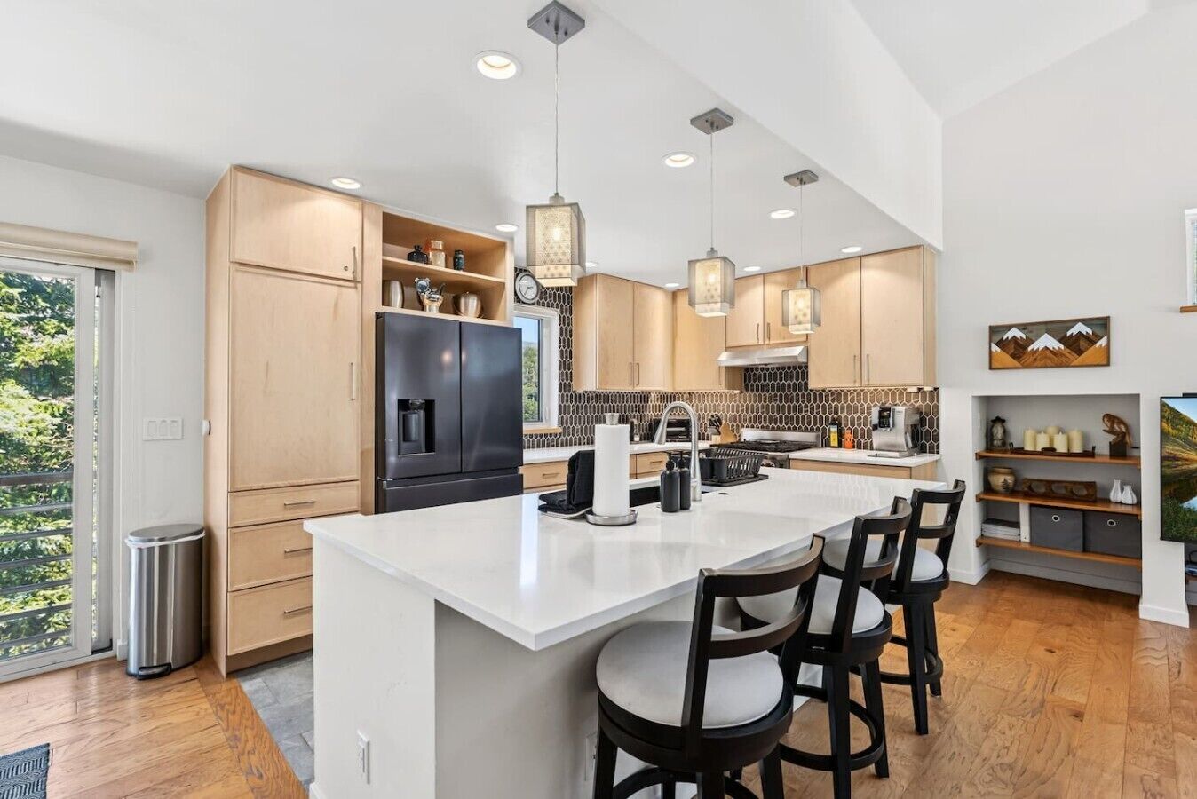 A modern kitchen with a large island, wooden cabinets, and pendant lighting.