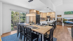 A modern kitchen with a central island, dining area with a large table and chairs, and a view of greenery outside. - Eagle Vail Mountain Retreat w/Fenced Yard (Avon)