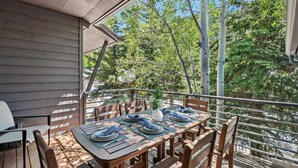 An outdoor dining area with a table set for four, surrounded by wooden chairs, on a balcony with a view of trees and a building. - Eagle Vail Mountain Retreat w/Fenced Yard (Avon)