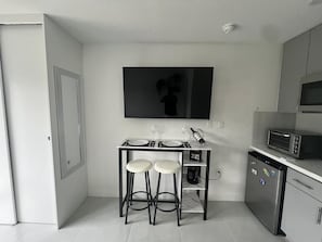 Eine kompakte Küche mit Fernseher, Mikrowelle, Toaster und einer kleinen Bar mit Barhocker.