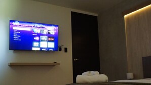 A modern hotel room with a flat-screen TV mounted on the wall, a bed with a wooden headboard, and a ceiling fan.