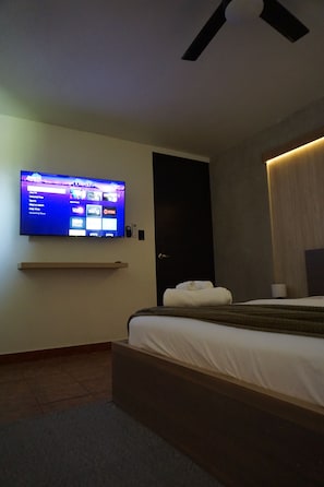 Une chambre d’hôtel moderne équipée d’un téléviseur à écran plat fixé au mur, d’un lit avec une tête de lit en bois et d’un ventilateur de plafond.