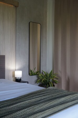 Une chambre d’hôtel avec un lit, une lampe de chevet, un miroir et deux plantes en pot.