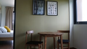 A room with a bed, two chairs, a table, and two framed pictures on the wall.