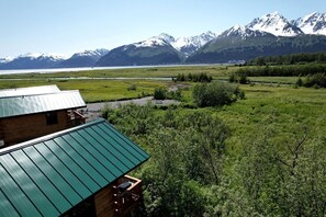 Un chalet rustique avec un toit végétalisé, offrant une vue sur une vallée, un lac et des montagnes.