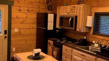 L'intérieur d'un chalet en bois comprend un coin cuisine équipé d'une table en bois, de tabourets, d'un réfrigérateur, d'un four à micro-ondes et d'une cuisinière.