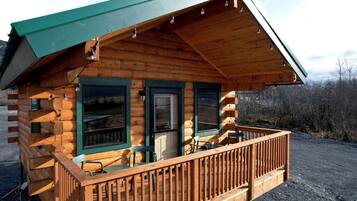 Une cabane en rondins avec une véranda, une porte et une fenêtre.