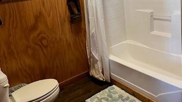 A wooden-paneled bathroom with a toilet, shower, and a small rug.