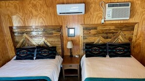Une chambre avec deux lits, des têtes de lit en bois, un appareil de climatisation, une lampe et une petite table.