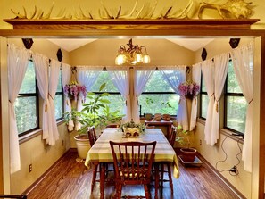 A dining area with a wooden table, chairs, a chandelier, and potted plants.