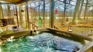 Ein Whirlpool mit einer Holzterrasse und Blick auf Bäume und einen Zaun.