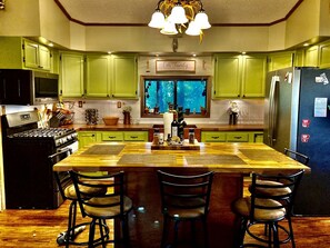 A kitchen with green cabinets, a wooden island, and a view through the window.