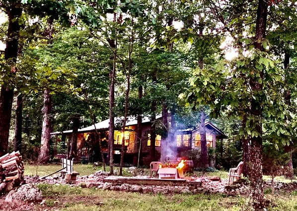 A rustic cabin with a fire, surrounded by trees.