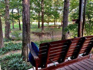 A wooden bench with a blue cushion in a wooded area with trees and a grassy field in the background. - Secluded Lakefront House Nestled in the Woods for an Unforgettable Adventure in Nature in Williford, Arkansas (Williford)