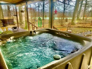 A hot tub with a wooden deck and a view of trees and a fence.