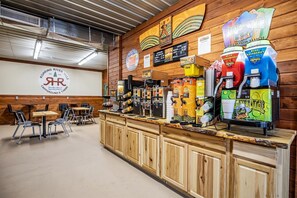 A rustic bar area with multiple beverage dispensers, a logo on the wall, and a seating area with tables and chairs. - Outstanding Tented Cabin with Fire Pit in Cassville, Missouri (Cassville)