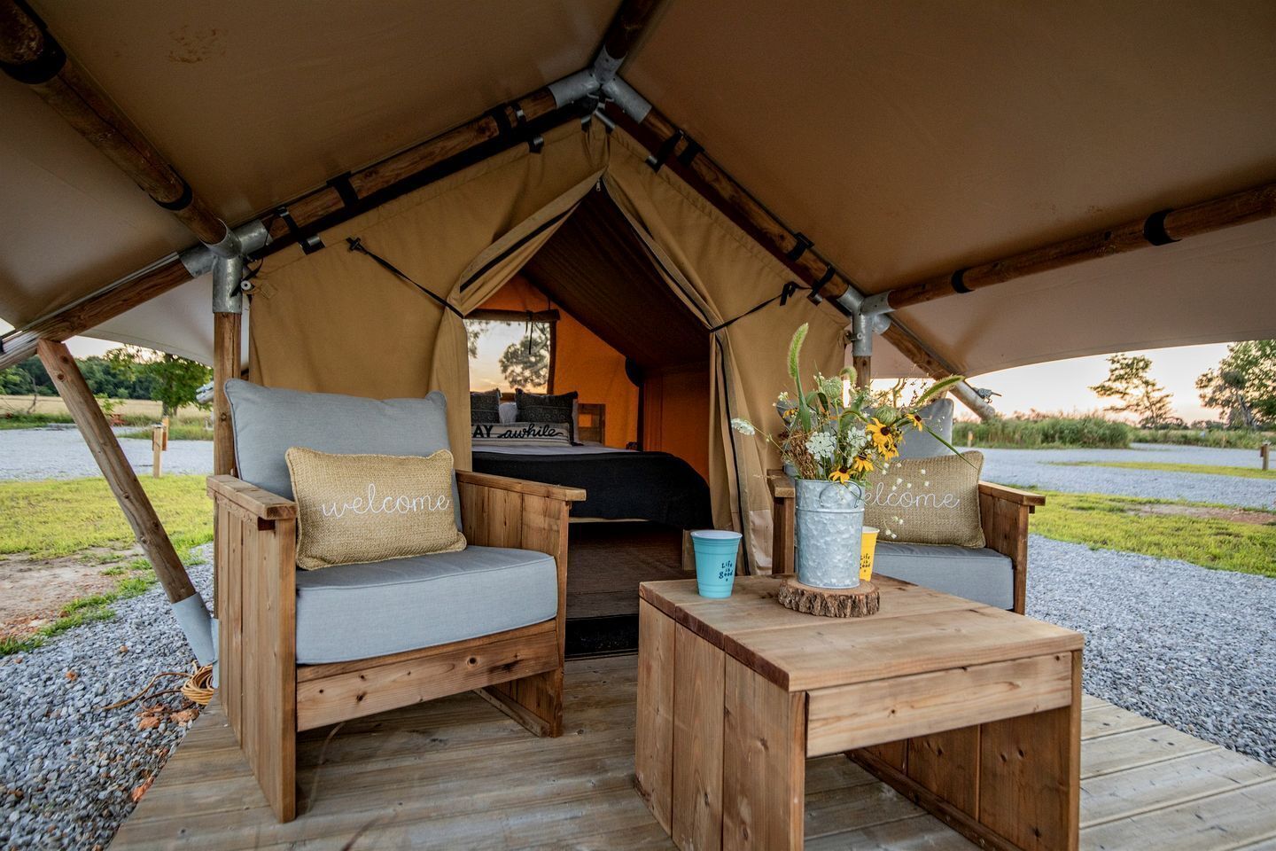 Un hébergement sous tente comprenant un lit, deux fauteuils confortables, une petite table avec un vase et une vue sur l’extérieur.