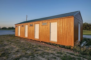 A wooden shed with a metal roof, a door, and windows, situated on a gravel path with grass. - Outstanding Tented Cabin with Fire Pit in Cassville, Missouri (Cassville)