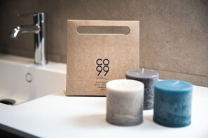 A bathroom sink with a modern faucet, a wooden bag with 'CO99' branding, and three candles of different colors. - CO99 - URBAN APARTMENT (Milano)
