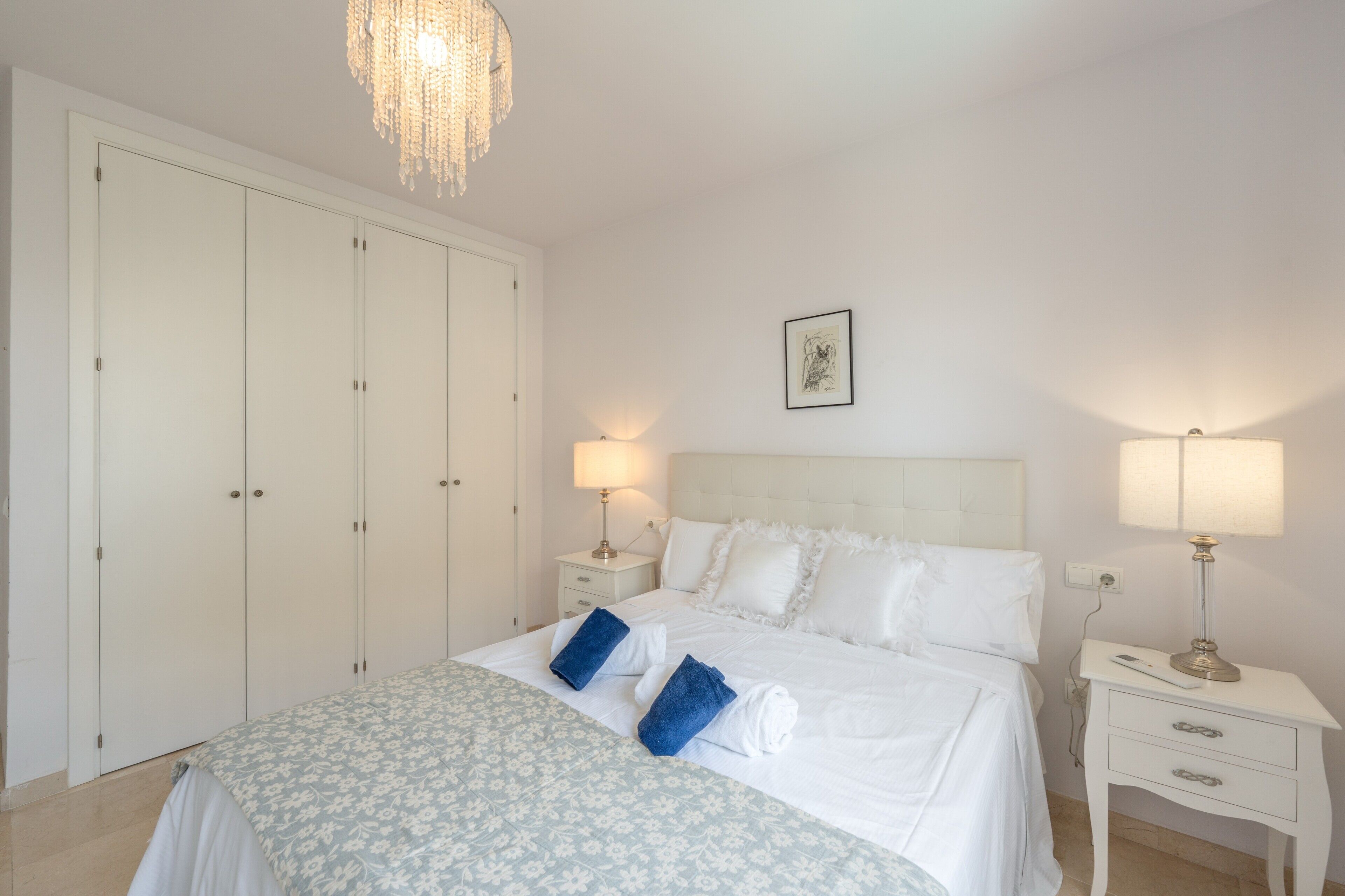 Een slaapkamer met een bed, nachtkastjes, een kroonluchter en een kledingkast.