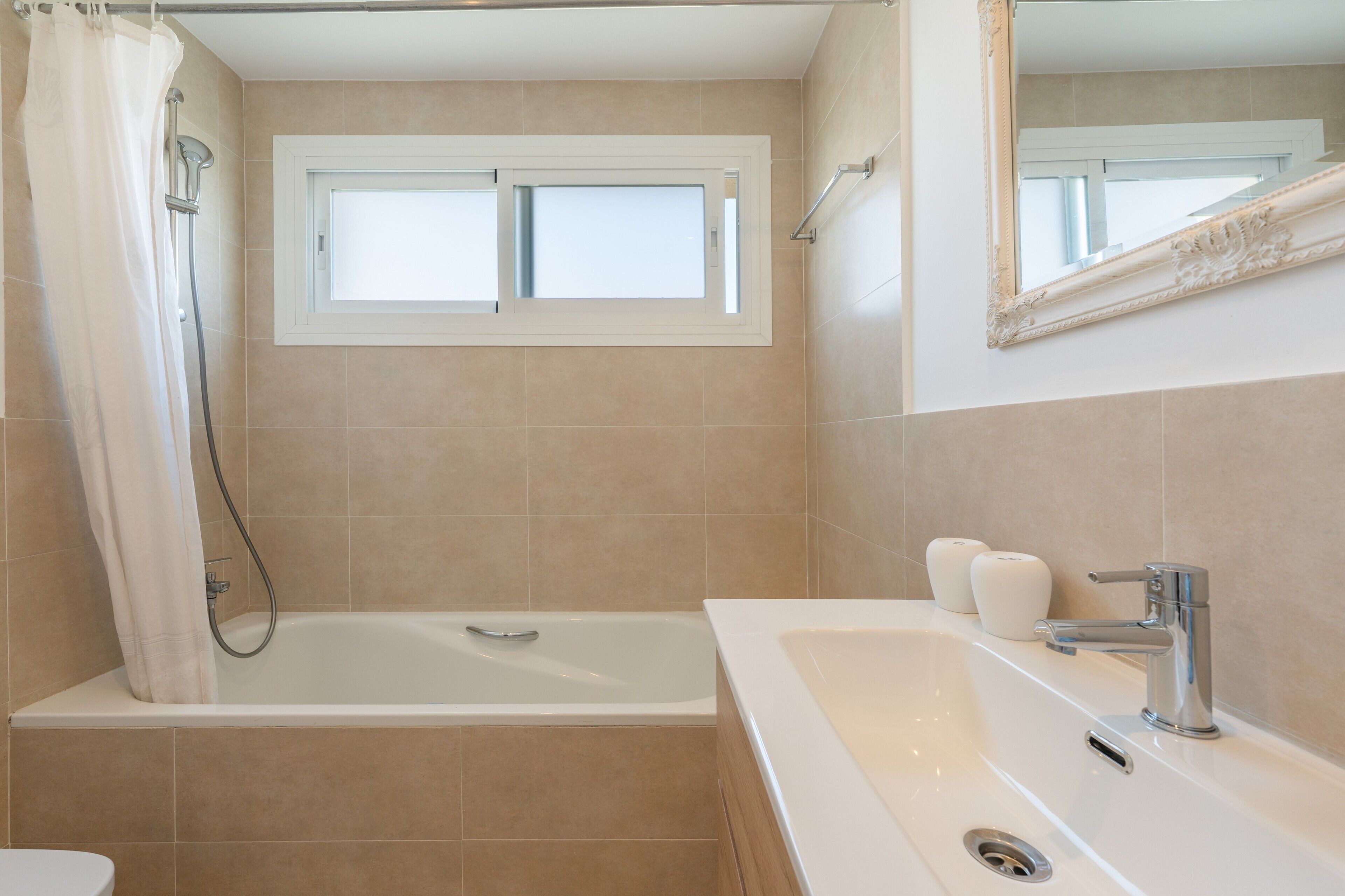 A bathroom with a bathtub, a window, a mirror, and a sink.
