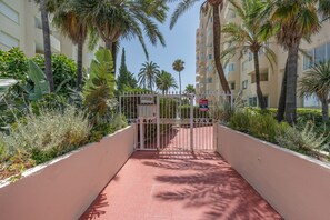 A gated entrance with a metal gate, palm trees, and a building with balconies in the background. - Apartment 'Balcon Del Puerto' with Sea View, Wi-Fi and Air Conditioning (Estepona)