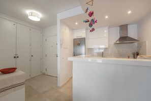 A modern kitchen with white cabinetry, a stainless steel range hood, and decorative fish wall art. - Apartment 'Balcon Del Puerto' with Sea View, Wi-Fi and Air Conditioning (Estepona)