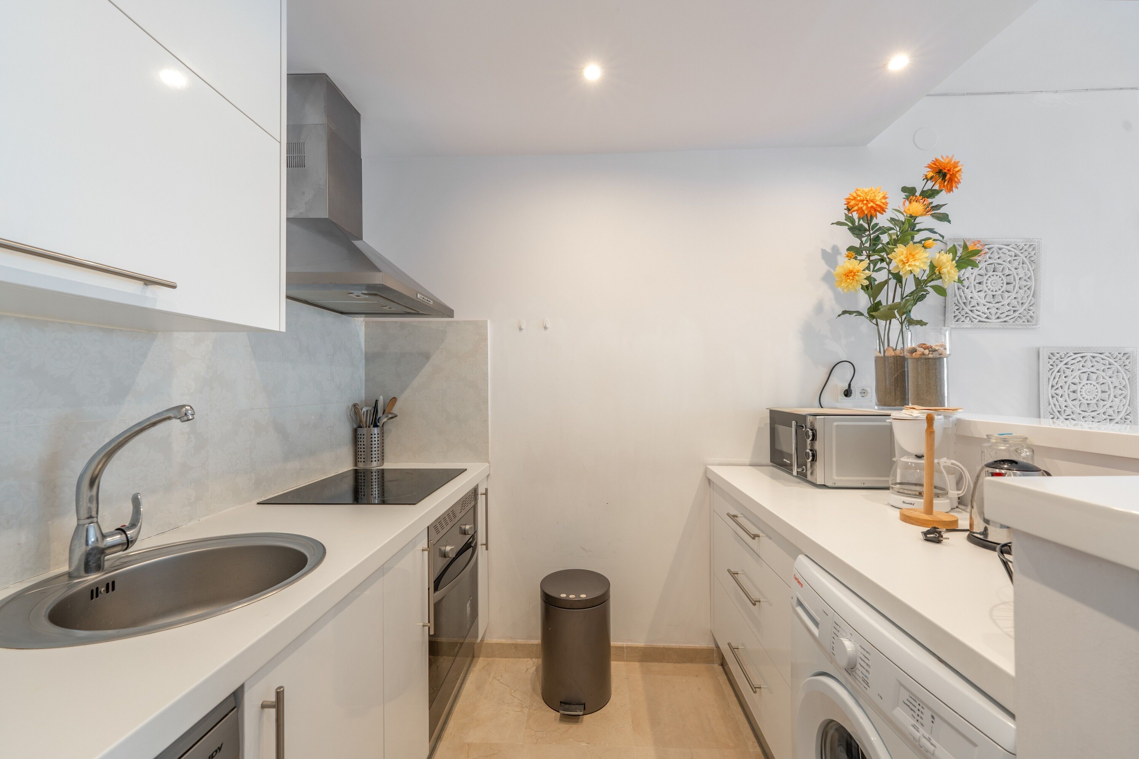 A compact kitchen with a sink, stove, microwave, and a small trash bin.