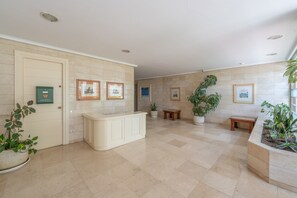 A spacious lobby with a reception desk, framed artwork on the walls, potted plants, and a tiled floor. - Apartment 'Balcon Del Puerto' with Sea View, Wi-Fi and Air Conditioning (Estepona)