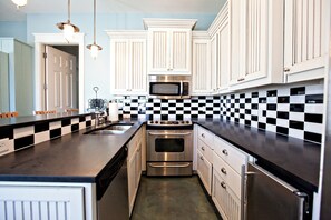 A kitchen with white cabinets, a black and white checkered backsplash, stainless steel appliances, and pendant lighting. - Nolan's Nook|Private Pool|Elevator|Golf Cart (Inlet Beach)