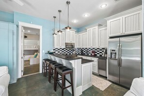 A modern kitchen with white cabinets, a stainless steel refrigerator, and a checkered backsplash. - Nolan's Nook|Private Pool|Elevator|Golf Cart (Inlet Beach)