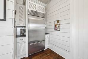 A kitchen with a stainless steel refrigerator, wooden cabinets, and a wooden floor. - Nolan's Nook|Private Pool|Elevator|Golf Cart (Inlet Beach)