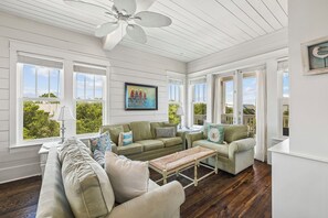 A sunlit room with a white ceiling fan, a green sofa set, a wooden bench, and a painting of children on the wall. - Nolan's Nook|Private Pool|Elevator|Golf Cart (Inlet Beach)