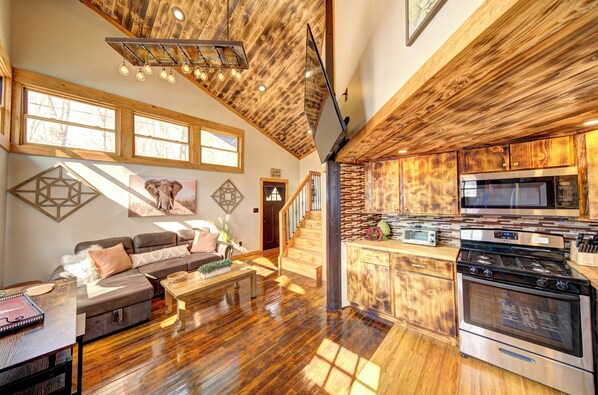 A spacious living area with a wooden ceiling, a kitchen with a large stove, and a staircase leading to another level.