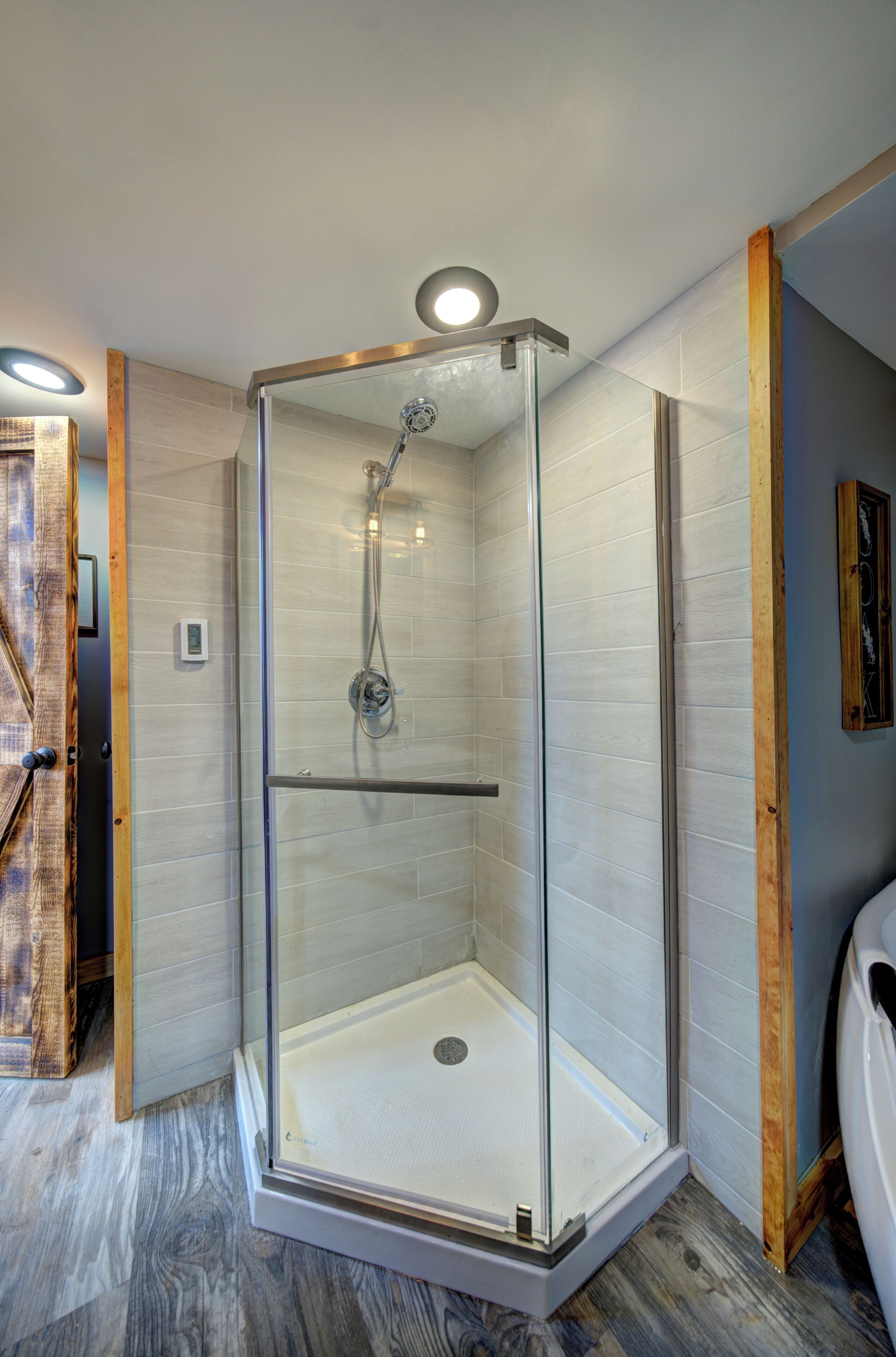 Eine begehbare Dusche mit Glaswänden, integriertem Sitzplatz, einer Leuchte darüber und Holzboden.