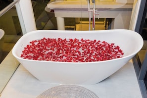 A white freestanding bathtub filled with red rose petals.