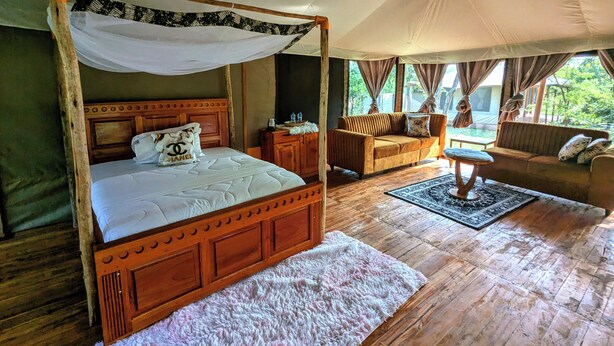 Un lit à baldaquin, un canapé, une petite table et un tapis dans une pièce dotée de parquets et de grandes fenêtres.