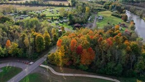 An aerial view of a campground with RVs, a river, and autumn foliage.