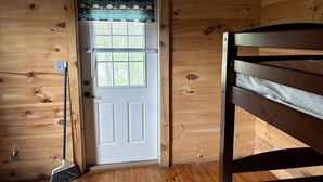 A wooden cabin interior with a door, a broom, and a bunk bed.