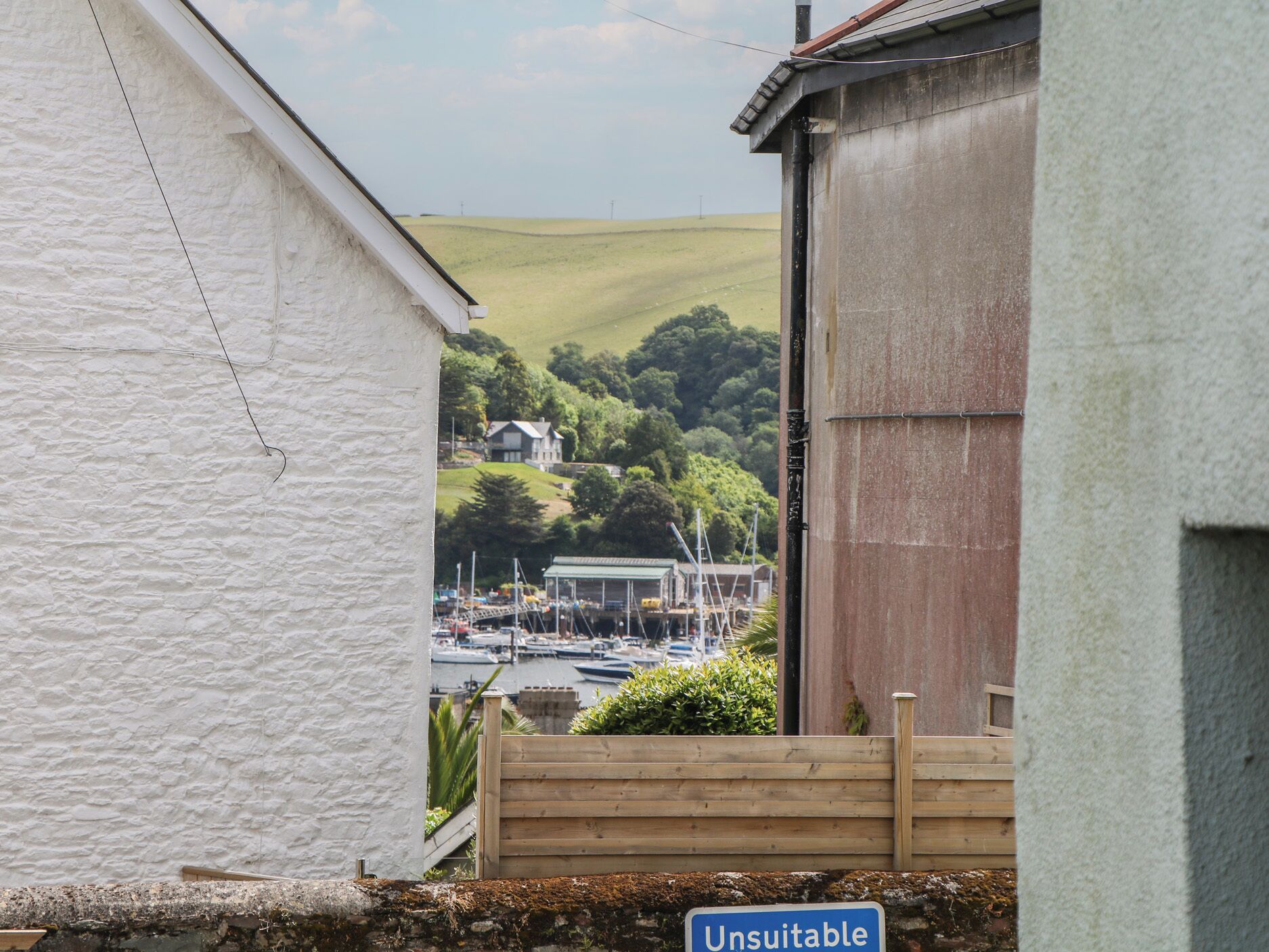 Une vue d’une marina avec des bateaux amarrés, un bâtiment sur lequel on peut lire l’inscription « Non adapté », et une colline en arrière-plan.