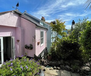 Ein rosafarbenes Haus mit Garten, einer Steinmauer und einem Winddreher.
