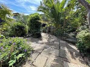 A stone pathway in a garden with various plants and a pergola structure. - Tiller Cottage (Dartmouth)